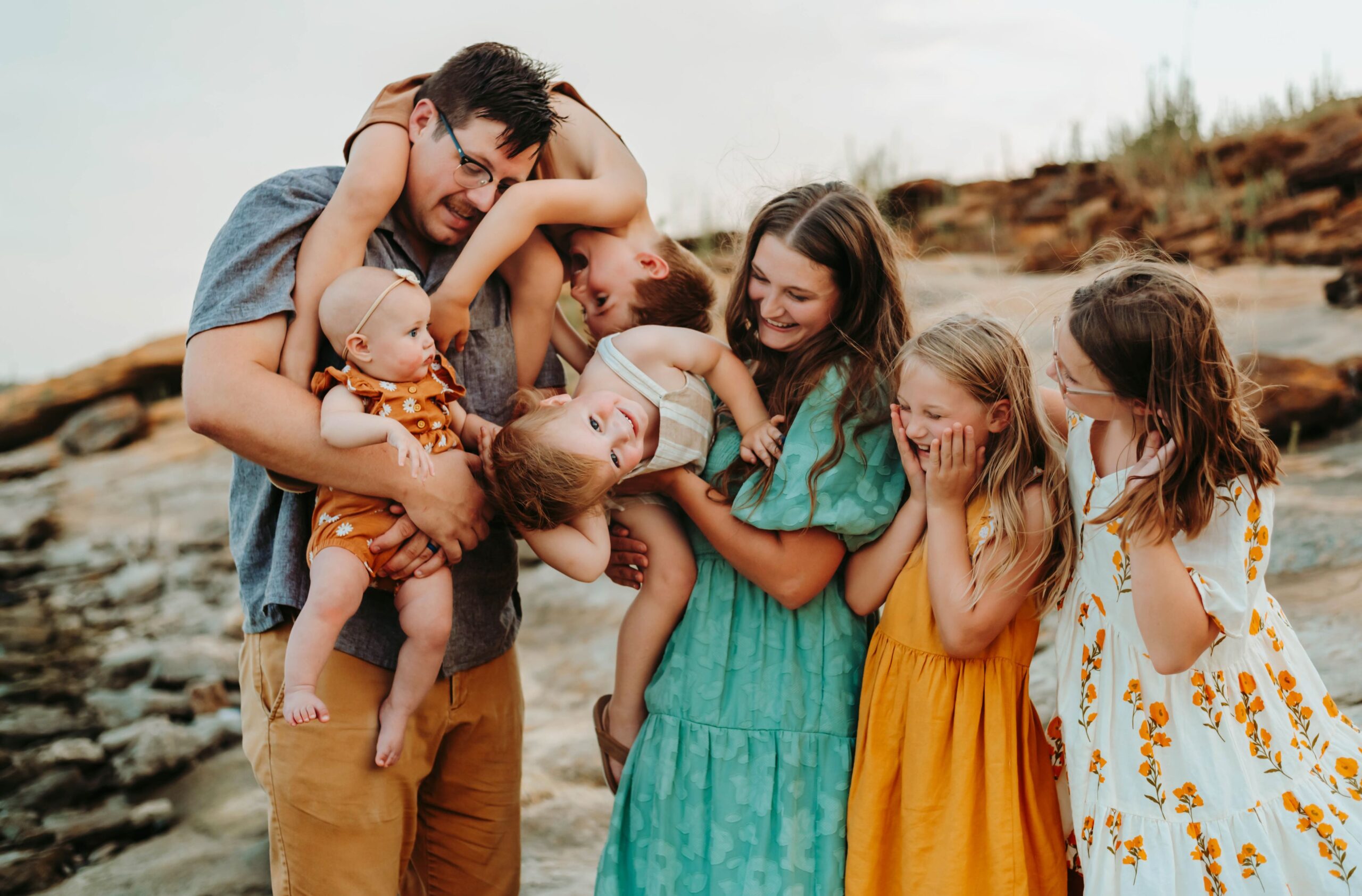 A joyful family moment captured by a Fort Worth family photographer on a rocky beach, with parents and children laughing together.